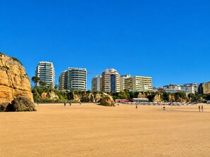A coastal cityscape with high-rise buildings, a sandy beach, and rocky cliffs.