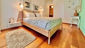 A bedroom with a wooden bed, a bedside table, a nightstand, a decorative rug, wall art, and a hanging light fixture.