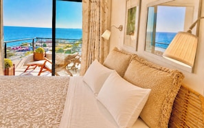 A hotel room with a large bed, a view of the sea, and a balcony with outdoor furniture.
