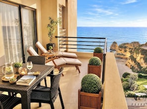 A balcony with a table set for dining, lounge chairs, and potted plants.
