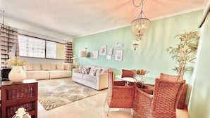 A living room with a sofa, a dining table with chairs, a chandelier, and a potted plant.