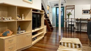 Un soggiorno moderno con un'unità d'intrattenimento in legno, una scala che conduce a un piano superiore e un'area pranzo con tavolo e sedie.