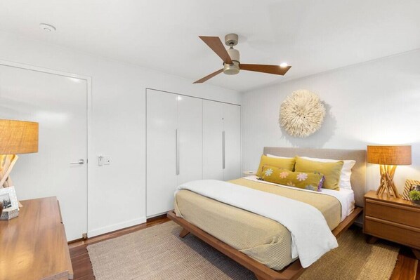 A bedroom with a bed, bedside tables, a ceiling fan, and a wall-mounted decorative piece.