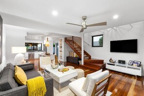 A modern living room with a sofa, coffee table, and a TV. There's a staircase leading to another level.