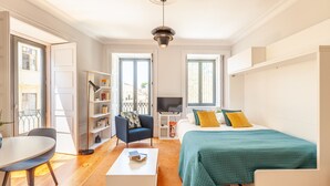 Une chambre moderne et bien éclairée, équipée d’un lit, d’un bureau, d’une chaise, d’une bibliothèque et d’un téléviseur.