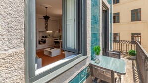 Un balcon avec une table et des chaises en verre, une plante en pot et une vue sur l’intérieur du bâtiment.
