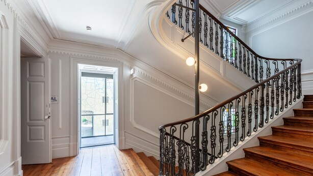 Un magnifique escalier, orné de rampes noires travaillées et de marches en bois, mène à une entrée lumineuse.