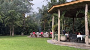 An outdoor seating area with a thatched roof pavilion, surrounded by lush greenery and a well-maintained lawn. - Tulivu Kilimanjaro Retreat (Moshi)