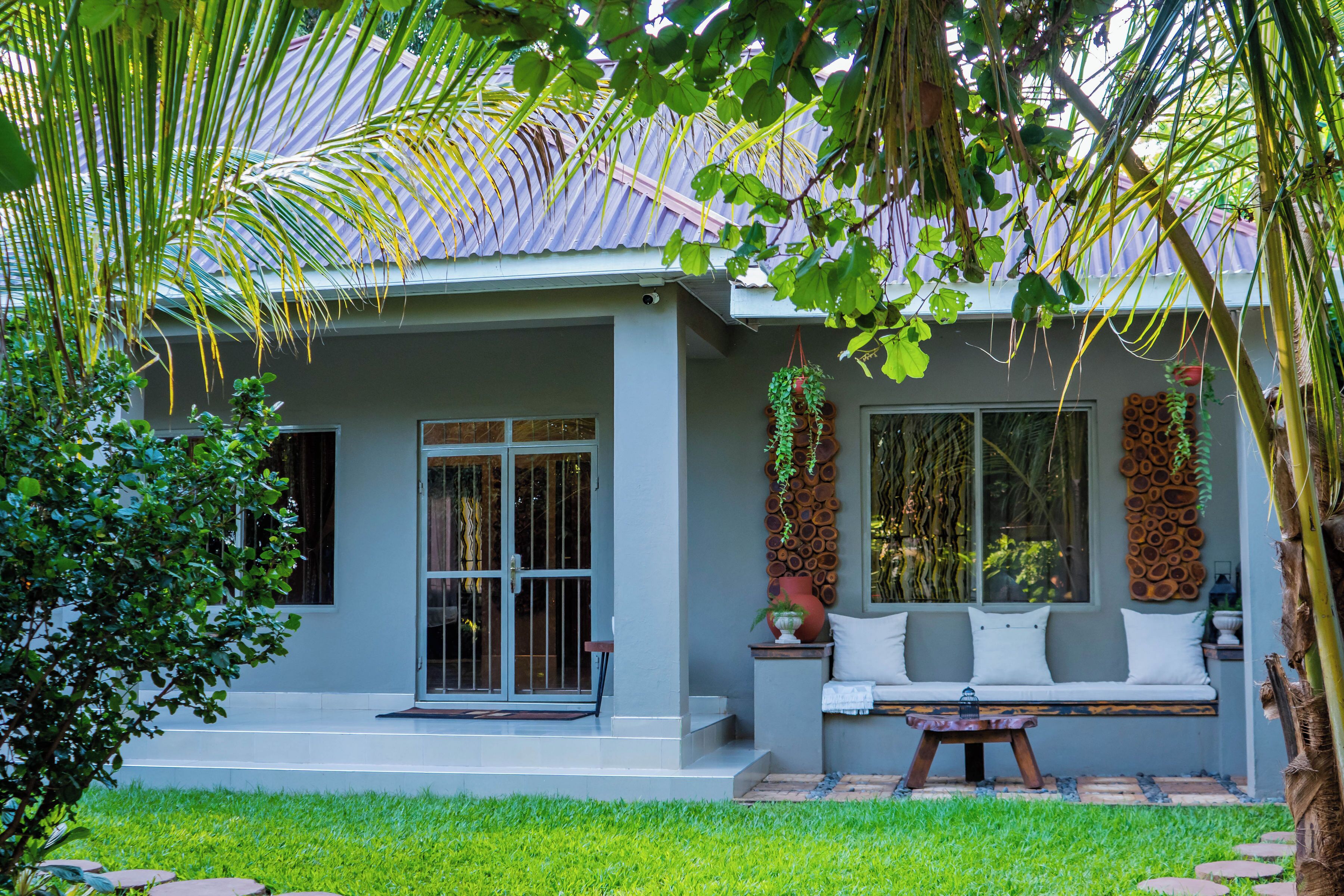 A house with a covered porch, a seating area with cushions, and a window with a view of the garden.