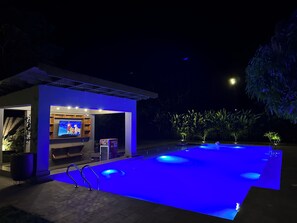 An outdoor swimming pool with blue lighting, a TV screen, and a sign that reads "Perfect Ice-Build." - Tulivu Kilimanjaro Retreat (Moshi)