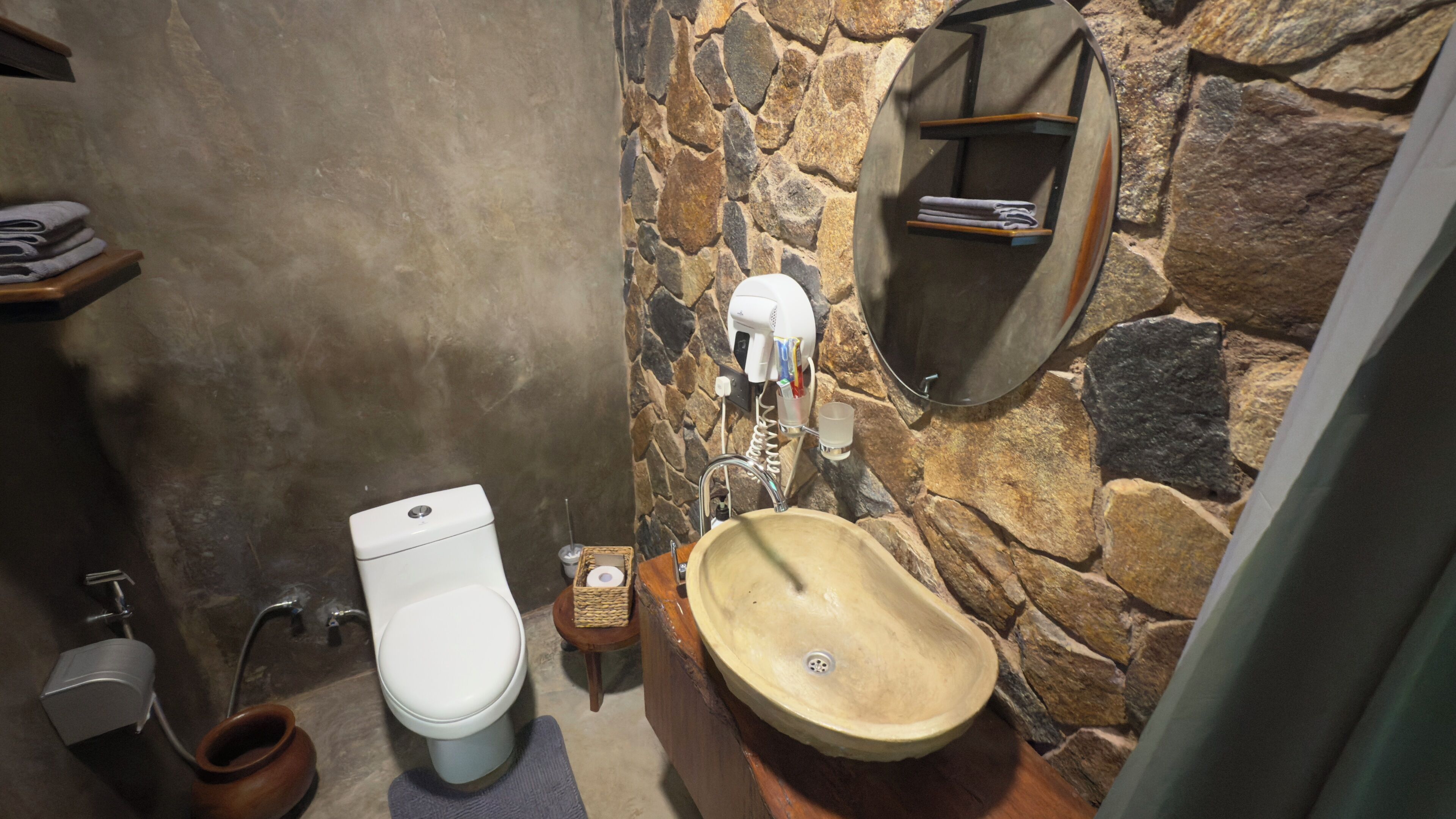 A bathroom with a stone wall, a wooden sink, a toilet, and a towel rack.