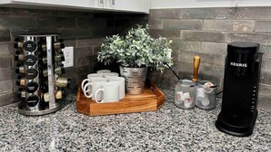 Un comptoir de cuisine avec un étagère à épices, une plante en pot, un plateau avec des tasses, une machine à café et un panier contenant des ustensiles.