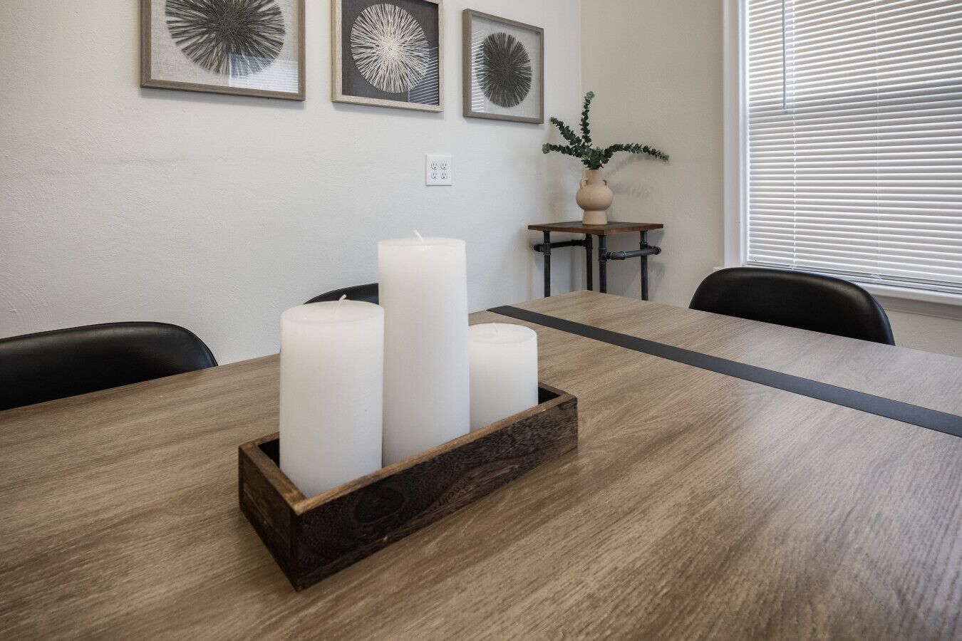 A conference room with a wooden table, three white candles in a wooden holder, and three framed abstract art pieces on the wall.