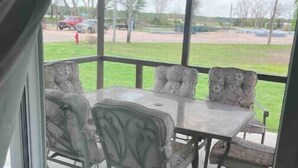 Eine überdachte Terrasse mit Tisch und Stühlen, Blick auf eine Rasenfläche und geparkte Autos.