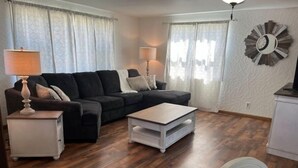 Ein Wohnzimmer mit einem dunkelgrauen Sofa, einem weißen Couchtisch und einem weißen Beistelltisch mit Lampe.