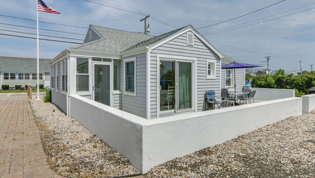 A single-story house with a covered patio, a flagpole, and a gravel driveway. - Cozy Westbrook Vacation Rental - Walk to Beach! (Westbrook)