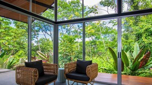 Ein modernes Zimmer mit großen Glasfenstern, Korbmöbeln und Blick auf üppiges Grün.
