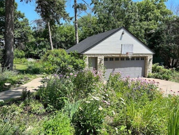 Situated in a lush garden, this charming structure offers a tranquil retreat with a garage door and pathway access.