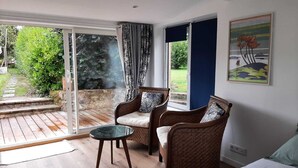 A room with a glass door leading to a patio, two wicker chairs with cushions, a small round table, and a bed. - Très Joli Studio, Neuf, à 50 m de la mer (Paimpol)