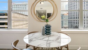 Un coin repas avec une table ronde en marbre, deux chaises, un vase de fleurs et un miroir encadré d’or accroché au mur.