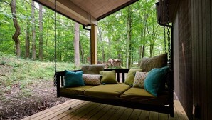 Une terrasse en bois avec un fauteuil suspendu, entourée d’une forêt.