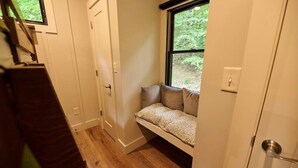 Un couloir étroit avec un banc intégré sous une fenêtre, une porte et un escalier.
