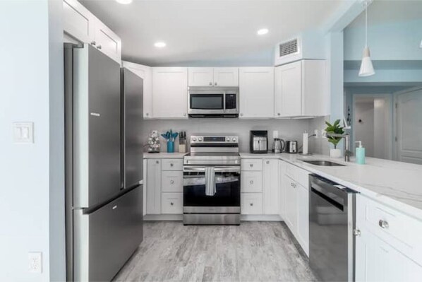 Features a sleek kitchen with stainless steel appliances, white cabinetry, and a sink and countertop area.