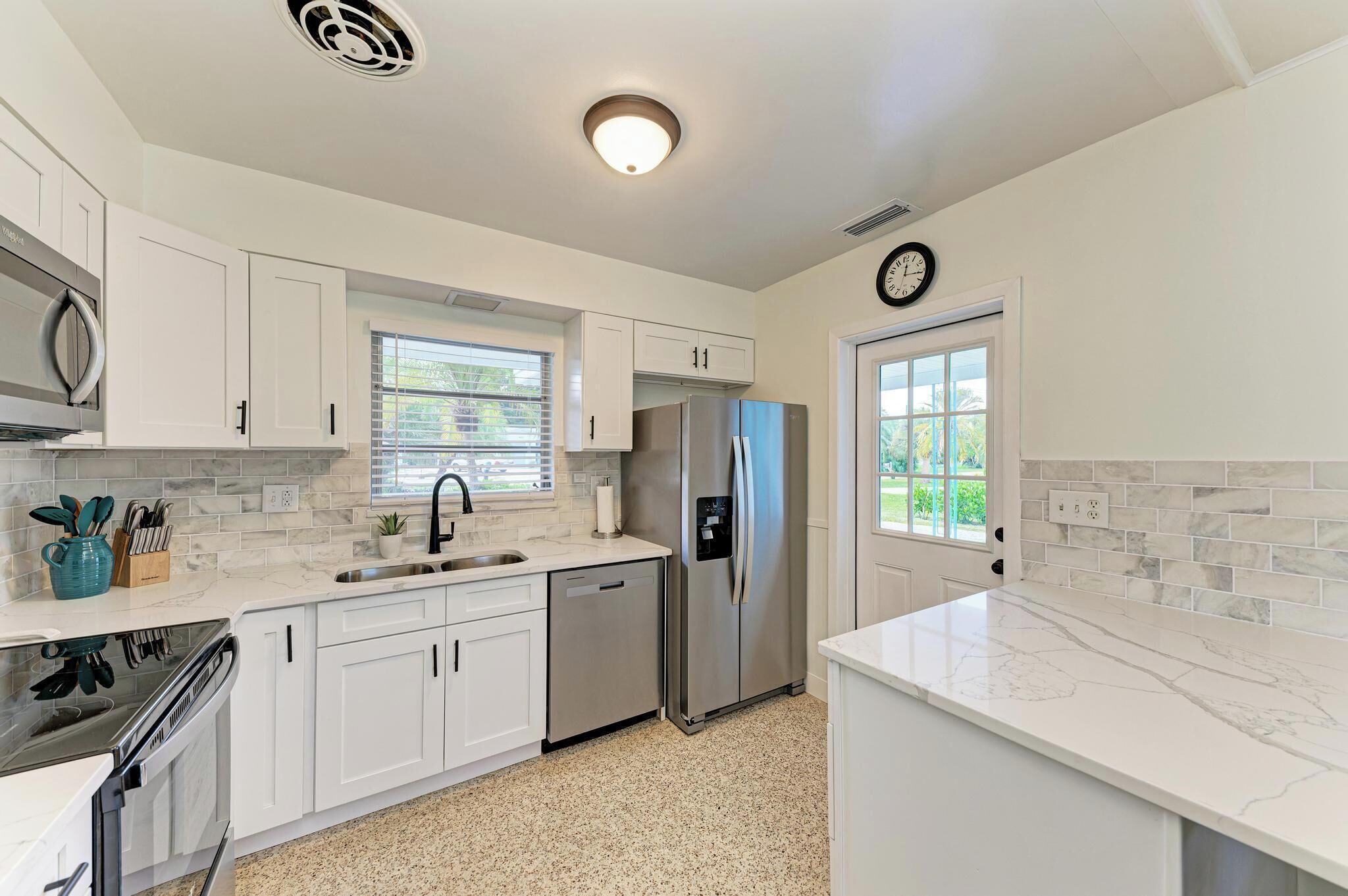 A modern kitchen with white cabinets, stainless steel appliances, and a marble countertop.
