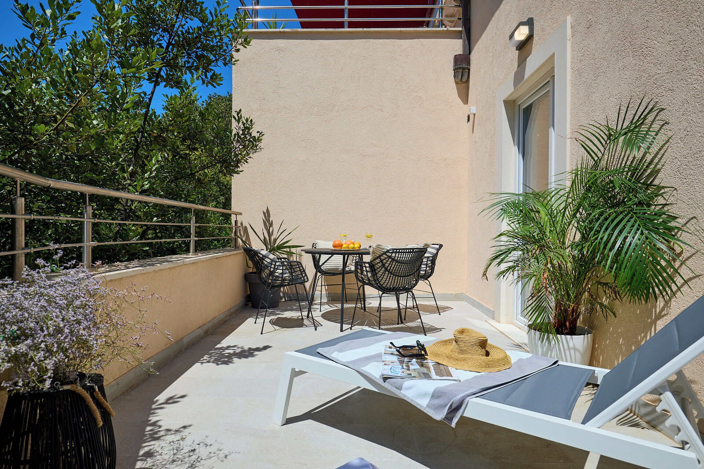 Un balcon avec une table et des chaises, un pot de fleurs et un fauteuil de relaxation.