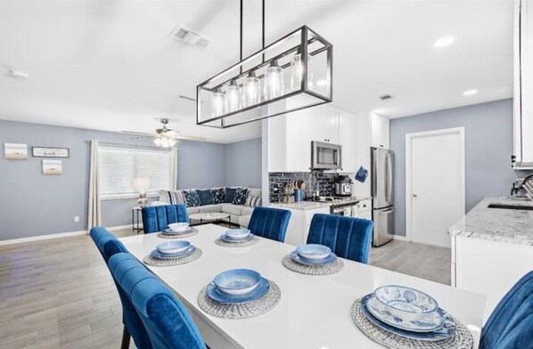 Un comedor moderno con una mesa blanca para seis personas, sillas tapizadas en azul y una lámpara colgante.