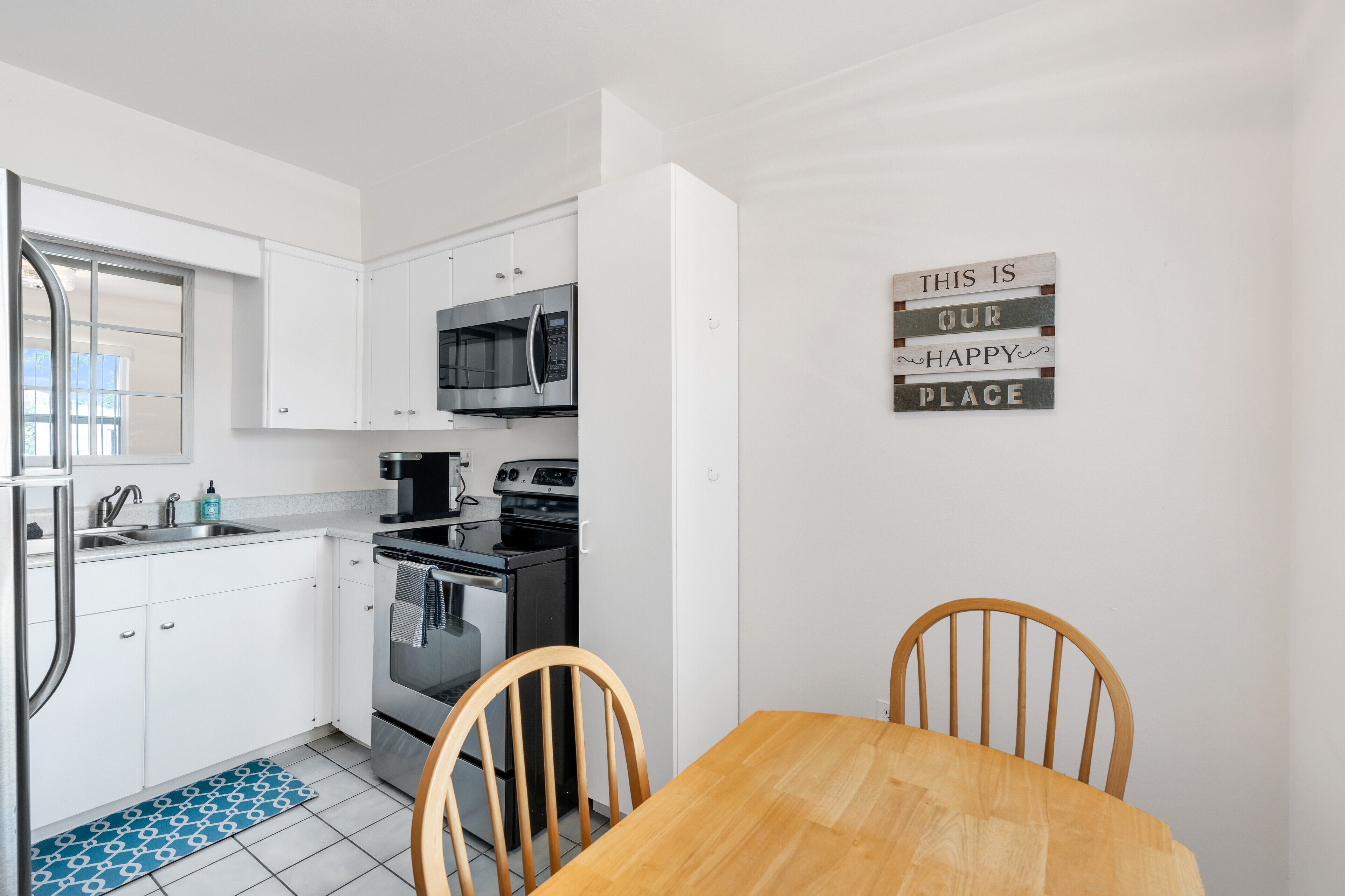 A modern kitchen with white cabinets, stainless steel appliances, and a wooden dining table.