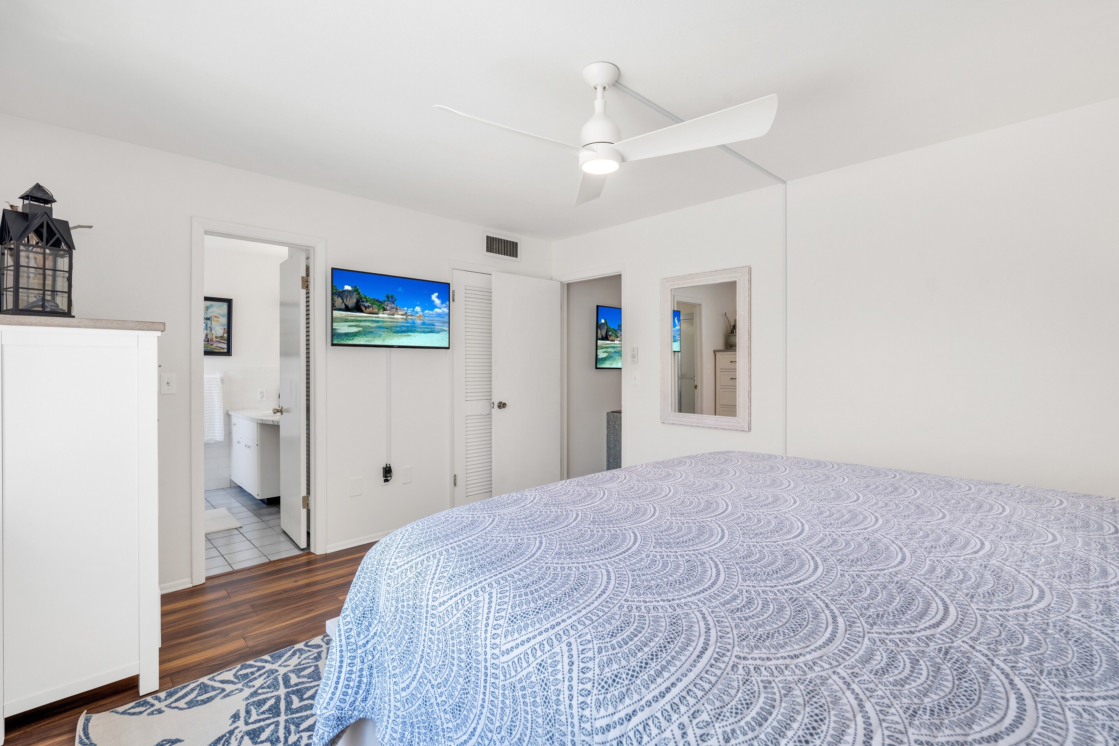 A bedroom with a bed, a ceiling fan, a painting, and a door leading to a bathroom.