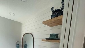 A bathroom with a white vanity, a mirror, and wooden shelves holding towels and a decorative item. - Venice Beach-Coco Palms 103. One block to Venice Beach.  (Venice)