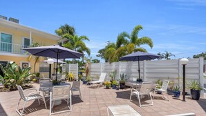 An outdoor patio with white metal chairs and tables, surrounded by potted plants and umbrellas. - Venice Beach-Coco Palms 103. One block to Venice Beach.  (Venice)