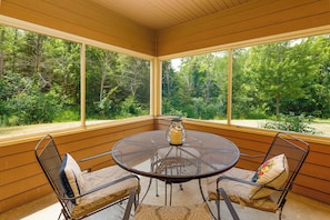 Enjoy a serene view of the lush forest from this sunroom, featuring a round table and comfortable seating for four.