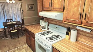 Une cuisine avec des meubles de rangement en bois, une cuisinière blanche, une machine à café et une table à manger avec des chaises.