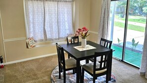 Un coin repas comprenant une table, des chaises, un vase avec des fleurs et une vue sur un jardin, visible à travers une porte-fenêtre coulissante.