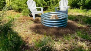 Deux chaises Adirondack blanches et un foyer en métal avec des bûches, le tout installé dans un espace extérieur verdoyant.