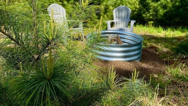Un espace extérieur accueillant, aménagé avec des fauteuils Adirondack et un foyer en métal, le tout entouré d’une végétation luxuriante.
