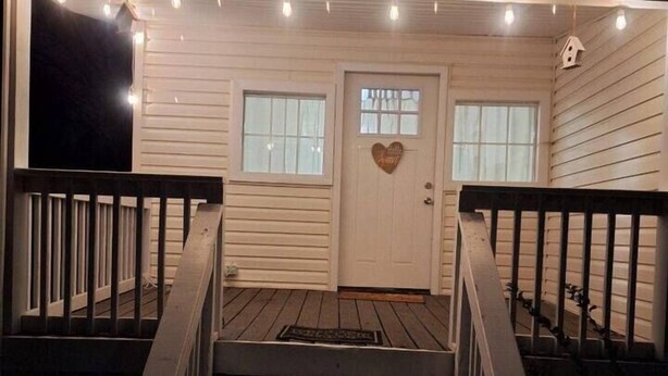 Un porche de madera con una puerta blanca, dos ventanas y un adorno con forma de corazón.