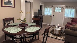 Un comedor con una mesa redonda y sillas, un televisor al fondo y una puerta que da a otra habitación.
