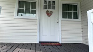 Una puerta blanca con un letrero con forma de corazón que dice 'Hello Love' y dos ventanas con cortinas.