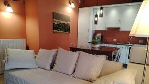 A bedroom with a sofa bed, a dining table, and a kitchen area with cabinets and a plant. - CASA CARMEN ( Sferisterio) near Parking (Macerata)