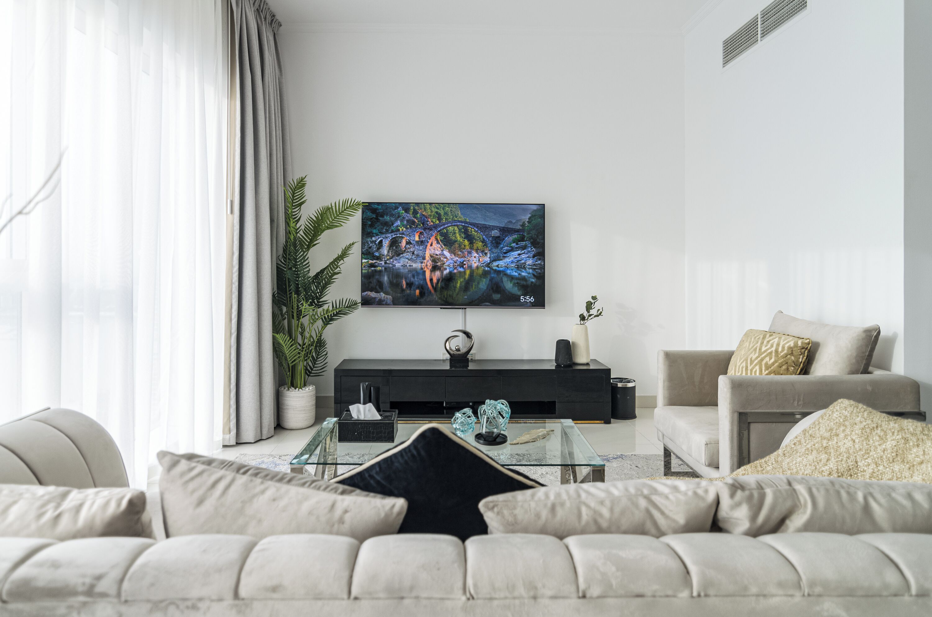 Ett modernt vardagsrum med en platt-TV som är monterad på väggen, en soffa, ett soffbord och en krukväxt.