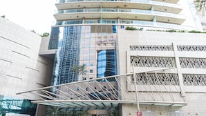 A modern building with a glass facade, a covered entrance, and a parking sign. - OSKENA Homes-Damac Heights Two Bedroom (Dubai)
