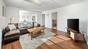 Un salon spacieux avec un canapé en cuir, une table basse en bois, un téléviseur à écran plat et un tapis à motifs.