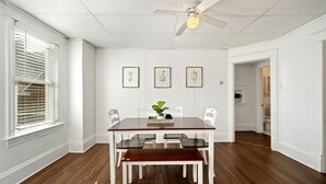 Une salle à manger avec une table en bois, des chaises blanches et un ventilateur de plafond.