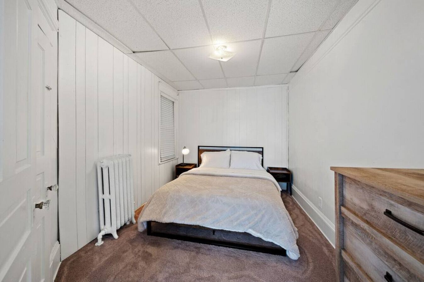 Et soveværelse med seng, kommode, radiator og dør.