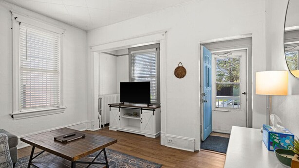 Un salon avec un téléviseur posé sur un meuble blanc, une table basse, un canapé et une porte donnant sur l’extérieur.