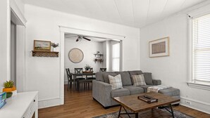 Un salon avec un canapé gris, une table basse en bois et un coin repas comprenant une table et des chaises.